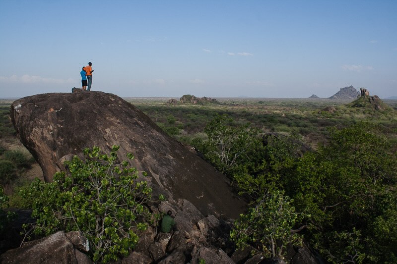Zwei Personen stehen auf einem Felsen der wie weitere Felsen aus der weitern Dornsavanne herausragt in Uganda