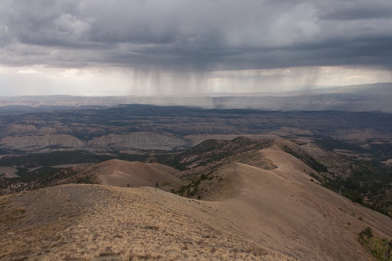 Bild über eine Ebene mit Hügeln in Utah mit dunklen Wolken und fallendem Regen in der Ferne