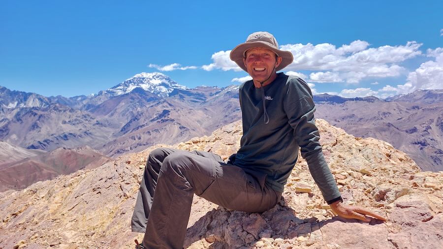 Gerald Klamer sitzt in Wanderkleidung auf einem Berggipfel in den Anden vor einer Kulisse aus weiten Bergketten