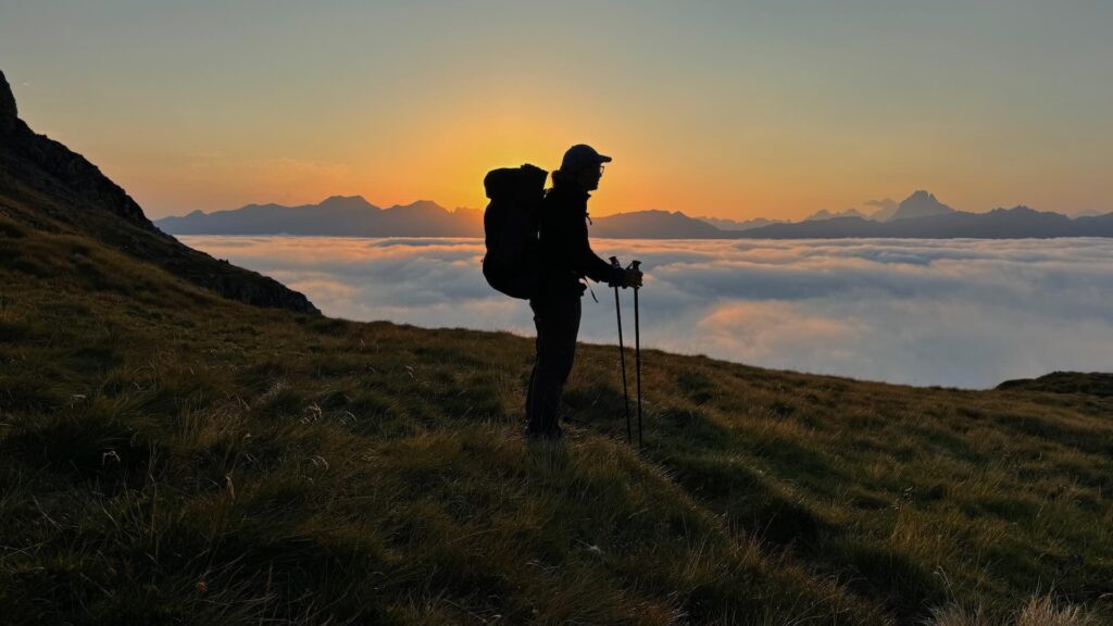 Die Silhouette eines Wanderers vor der aufgehenden Sonnen über einem Wolkenmeer in den Bergen