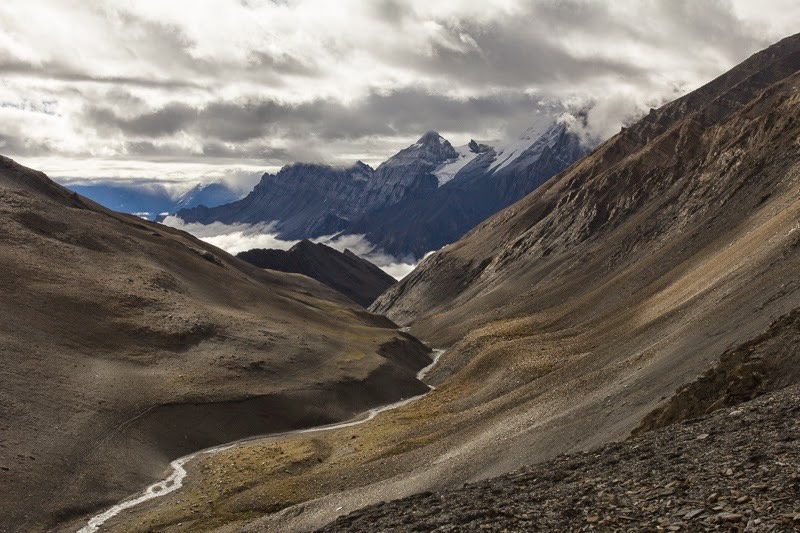 Blick in eine trockene Landschaft mit Bach und Bergen im Hintergrund in Nepal
