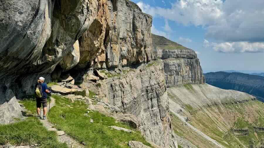 Wanderer läuft entlang eines smalen Bandes an einer steilen Felskante in den Pyrenäen