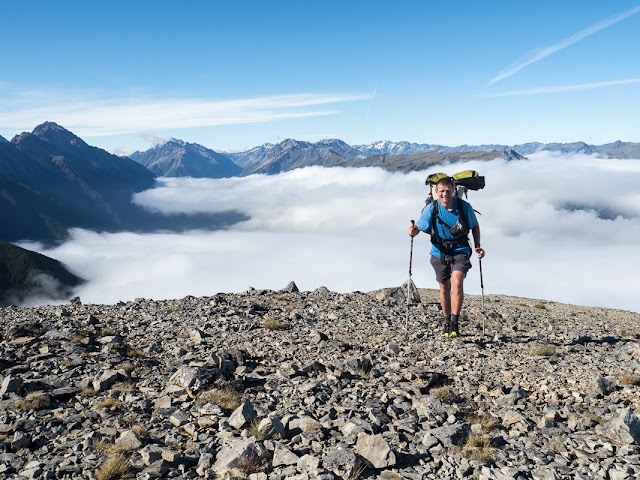 Wanderer mit Rucksack läuft über einem Wolkenmeer in den Bergen in Neuseeland